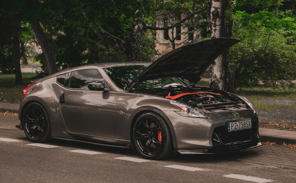 A sleek luxury sports car with an open hood parked by the roadside in a lush green area.